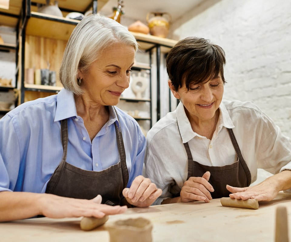 Two women working side by side at a pottery bench, both concentrating and smiling