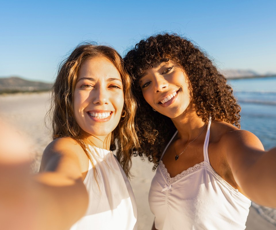 Two women standing together outdoors on a bright day, laughing
